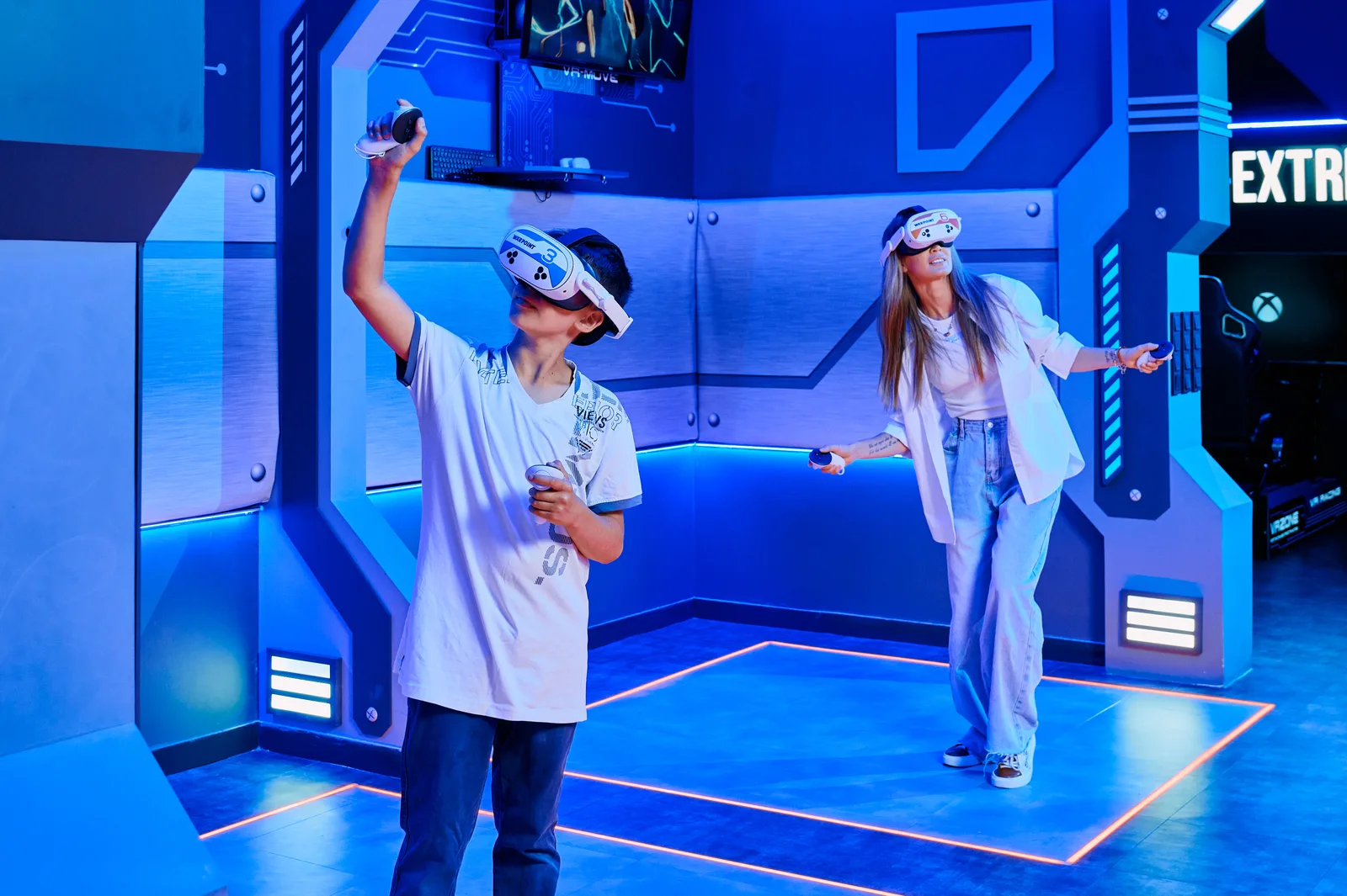 Ана мен ұлы VR-шлемде еденінде жарықтандырылған аймақтары бар ВР Станцияда ойнап жатыр
